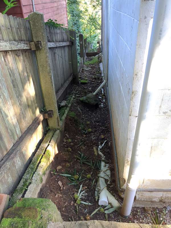Photo of region 5a down the side of the house showing a dark, mucky area enclosed between a white masonry wall and wooden fence